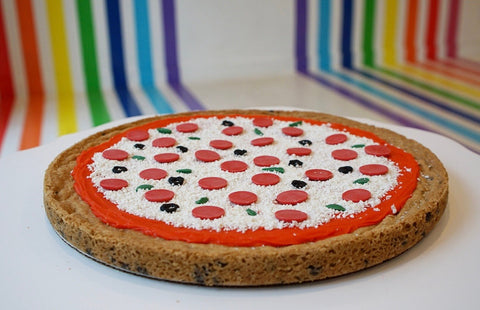 Mega Cookie Cake decorated to look like a pizza with rainbow background